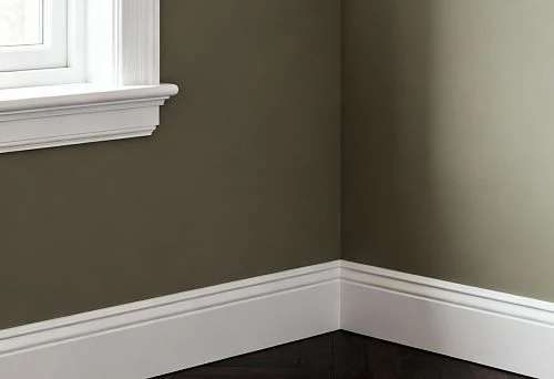 Interior corner with installed plastic skirting board and windowsill, demonstrating neat joint finishing and clean floor junction line