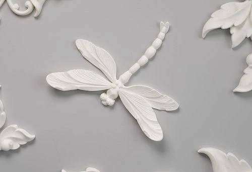 Decorative polyurethane ceiling molding: relief dragonfly, floral ornaments, elegant leaves and flowers on a light gray background.