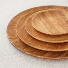 Round wooden plate with nuts and dried fruits on a linen tablecloth.